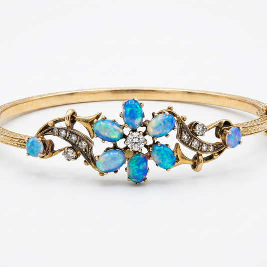 A gold hinged bangle bracelet featuring a central floral arrangement of blue opal gemstones and small clear diamond stones, set against a plain white background.