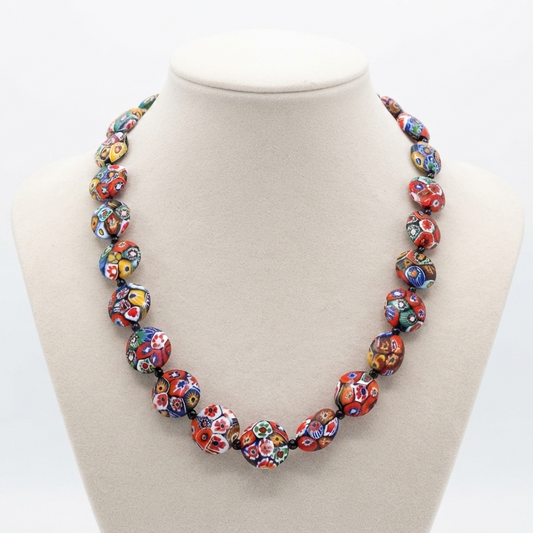 A colorful beaded necklace displayed on a cream-colored jewelry bust against a white background. The necklace features multiple round beads, each decorated with a vibrant, multicolored floral and geometric pattern.