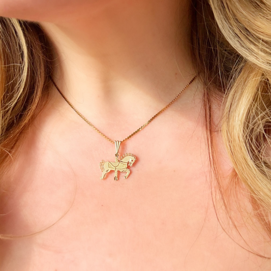 A close-up of a model wearing a delicate gold necklace with a small horse-shaped pendant.