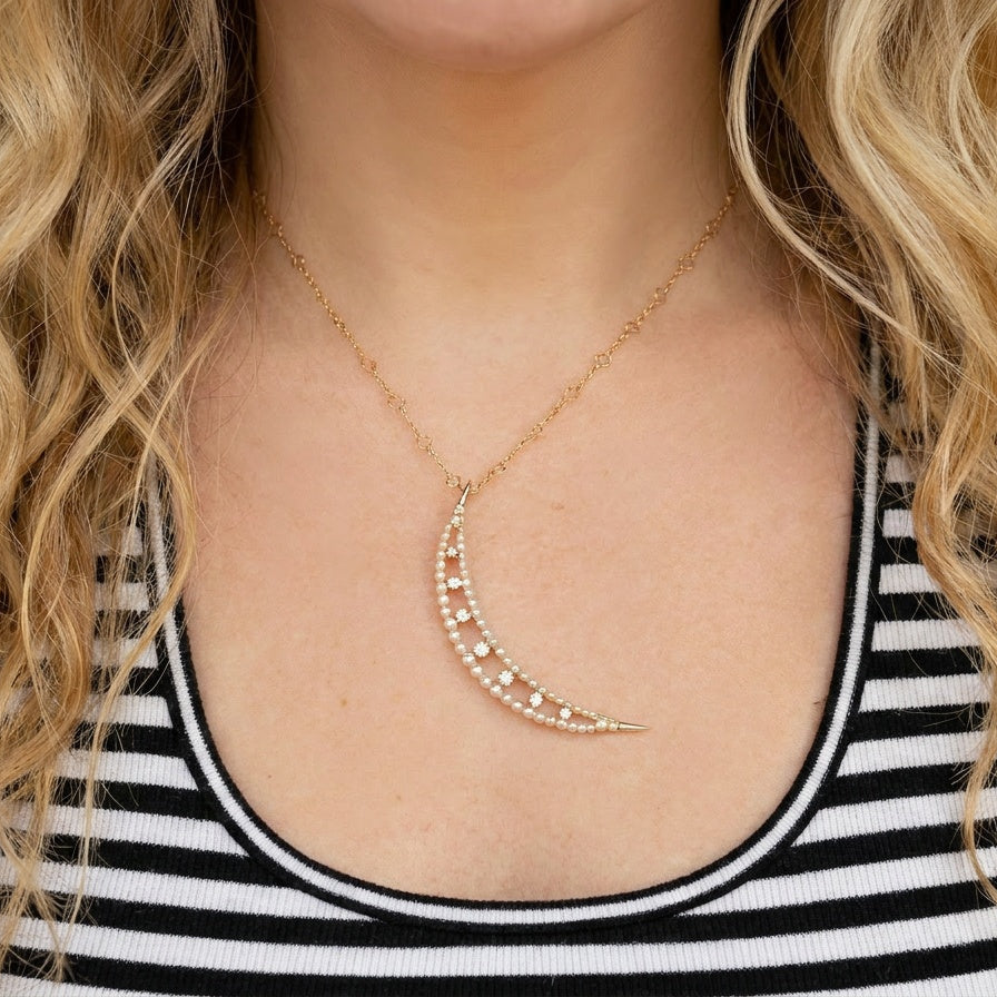 Person wearing a gold necklace with a crescent moon pendant, against a neutral background.