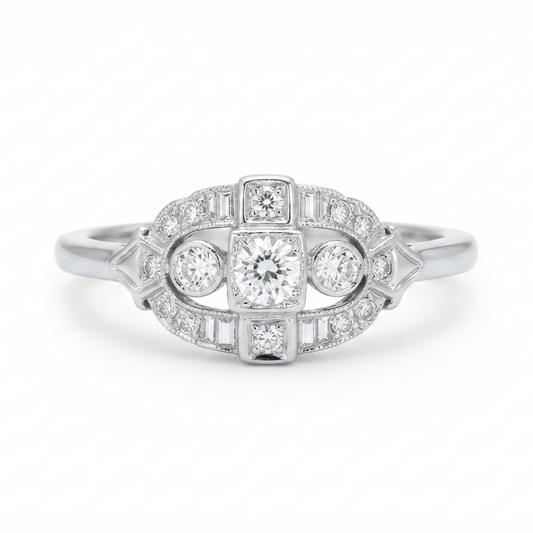 An Art Deco diamond ring in a white gold metal, featuring a central round diamond surrounded by smaller baguette and round-cut diamonds, set against a plain white background.