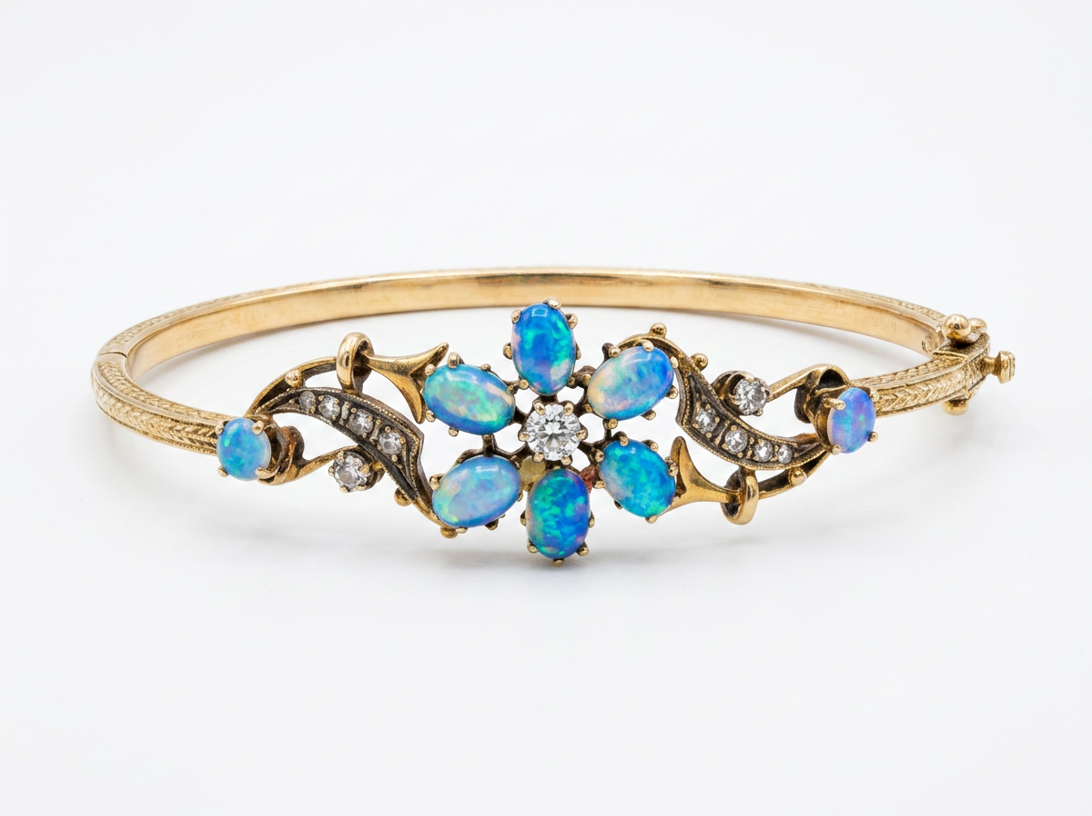 A gold hinged bangle bracelet featuring a central floral arrangement of blue opal gemstones and small clear diamond stones, set against a plain white background.