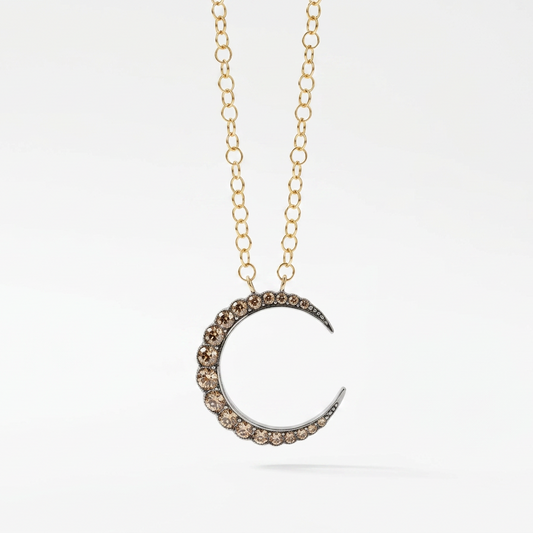 A gold chain necklace with a crescent moon pendant adorned with small clear paste gemstones on a clean white background.