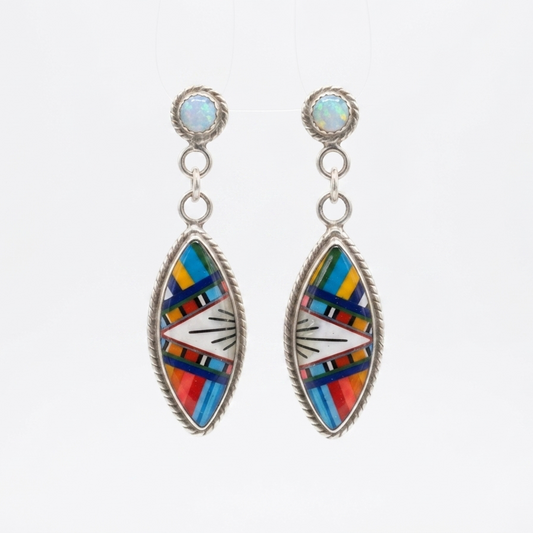 A pair of silver dangle earrings with oval bezel settings featuring a colorful Southwestern-style inlay pattern of blue, red, yellow, green, and white, suspended against a plain white background.