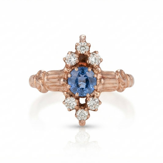 A rose gold ring featuring a central oval blue sapphire surrounded by a halo of small round diamonds, with a textured band, set against a plain white background.