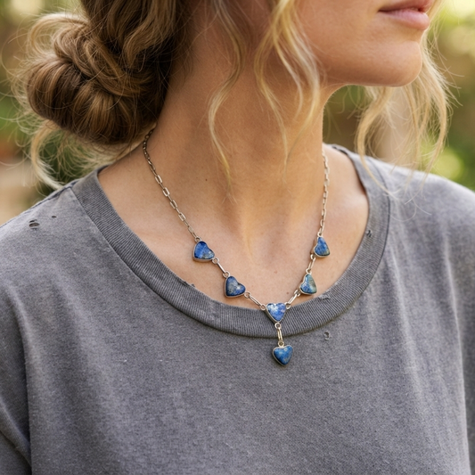 A close-up lifestyle shot of a woman wearing a silver chain necklace with multiple small blue heart-shaped pendants and a larger dangling blue heart at the center.