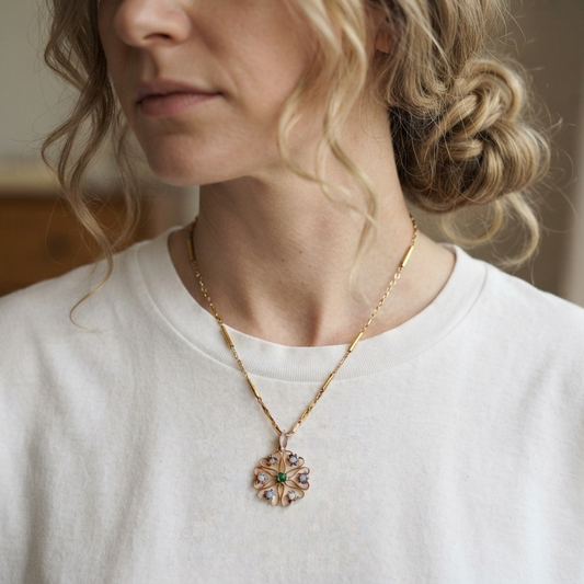 A close-up shot of a woman wearing a delicate gold chain necklace with a colorful floral pendant, paired with a white crewneck t-shirt.